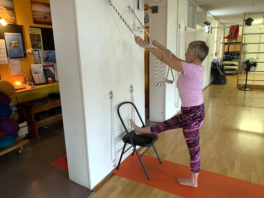 Chris in a standing pose with one foot on a chair and the hands on wall ropes