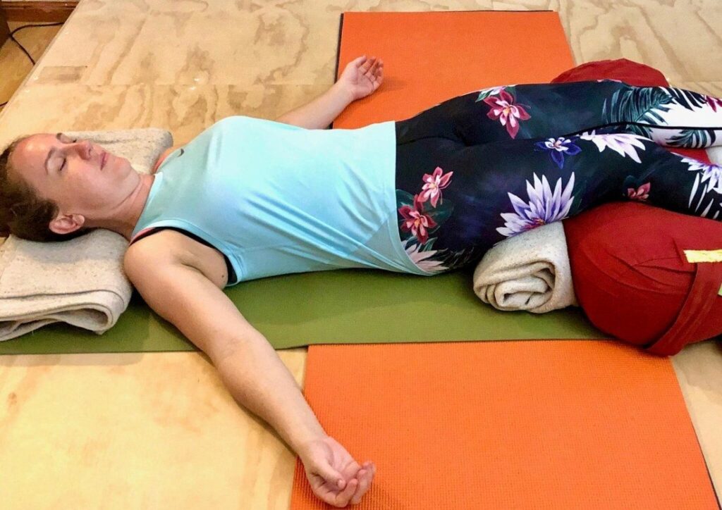 Sore back yoga Darwin: a student resting on blankets and a bolster at the end of a gentle Iyengar class