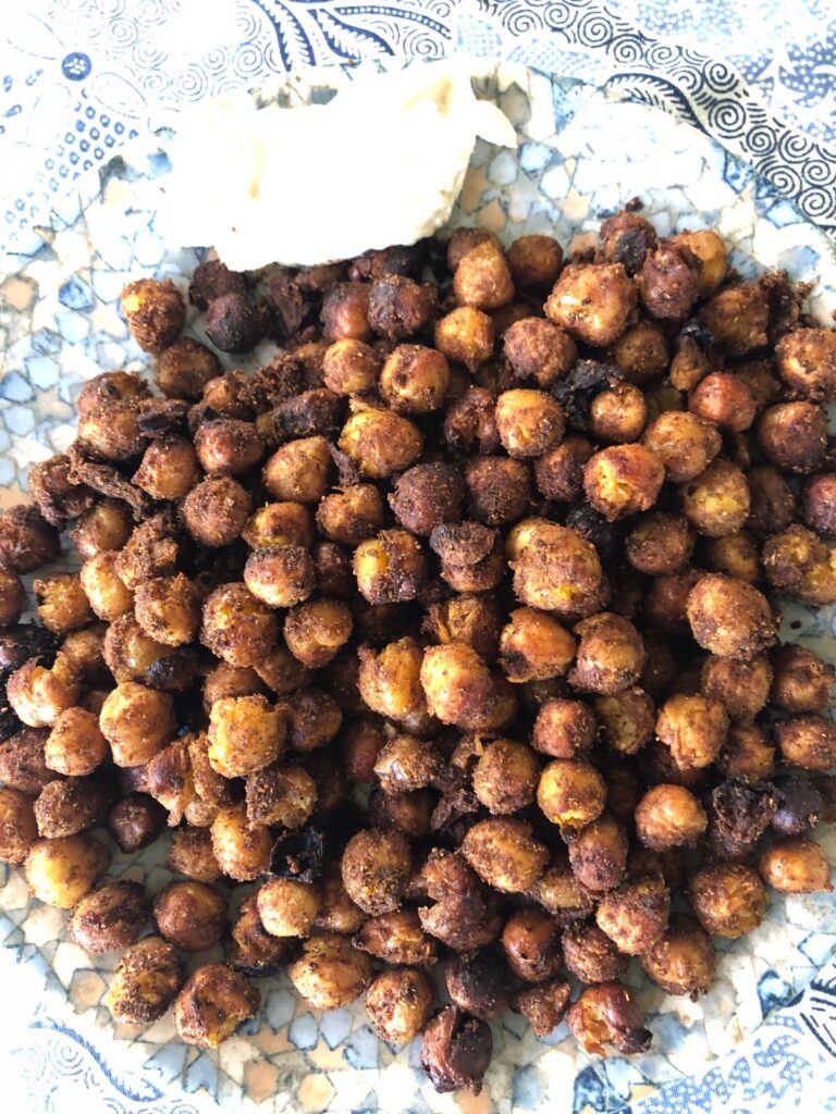 A plate of spicy roasted chickpeas, dark and crunchy, with a spoonful of hummus on a blue and white cloth
