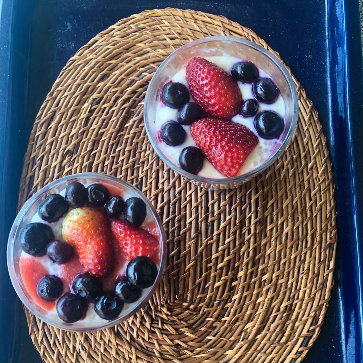 Two glasses of strawberry tapioca pudding topped with strawberries and blueberries