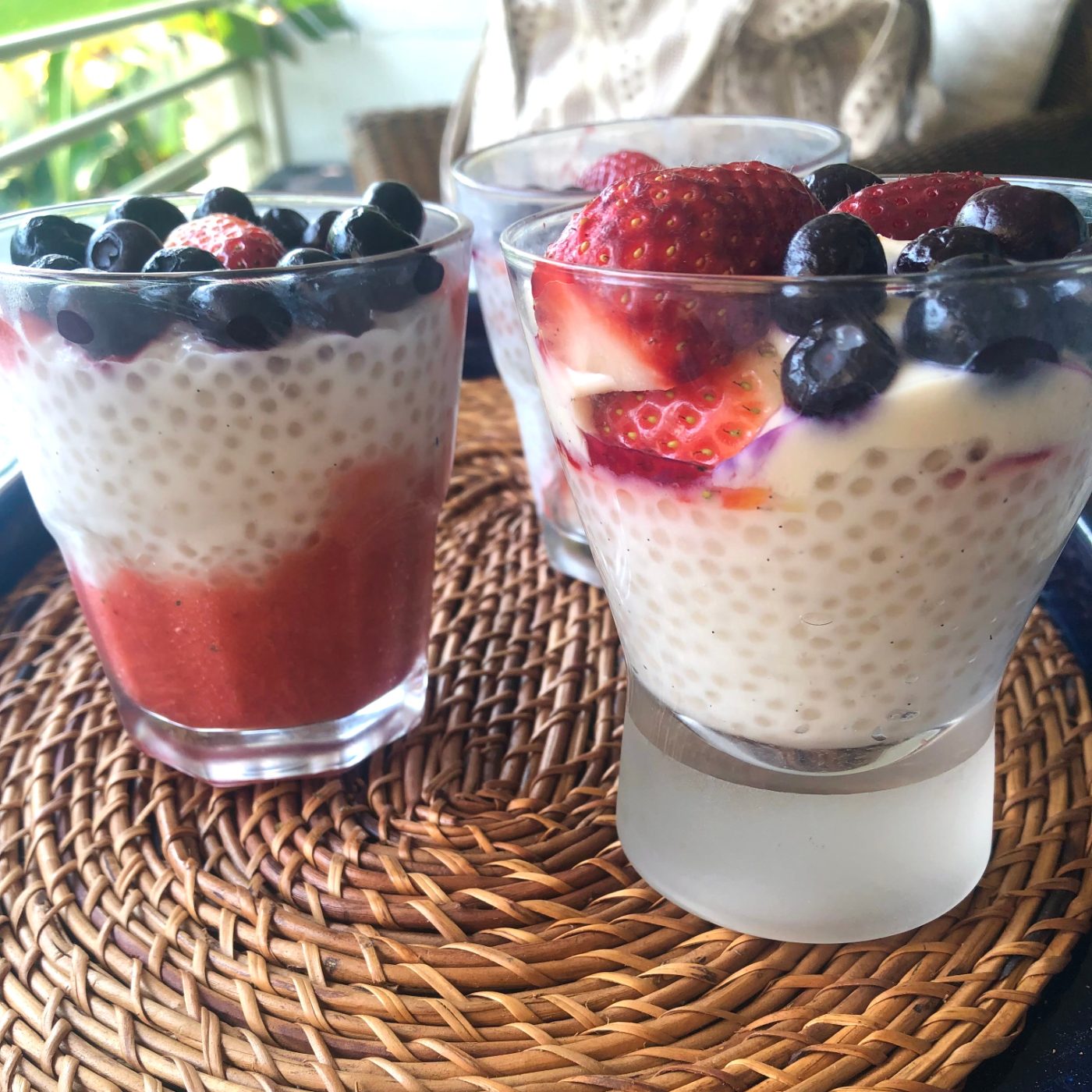 Strawberry tapioca pudding in a glass showing layers of strawberry puree, tapioca in coconut milk, strawberries and blueberries
