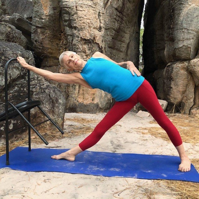 Tight hips Darwin: a woman in a wide standing pose beside a chair on a beach, back leg long, hips working