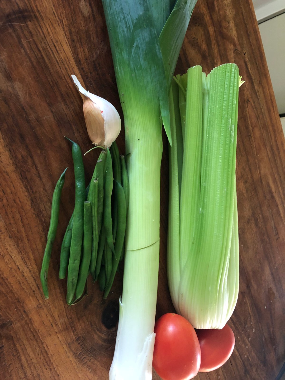 Tomato soup ingredients on a wooden board: leek, celery, green beans, garlic and ripe tomatoes