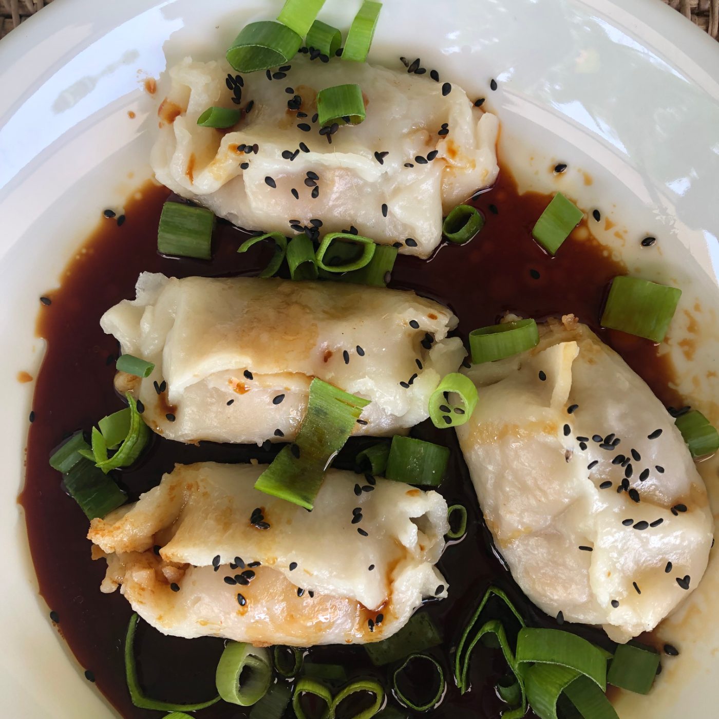 Close up of vegan tofu wontons in soy and mirin dipping sauce with spring onions