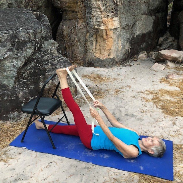 Yoga for flexibility Darwin: a lying leg stretch with a belt, one leg straight up, the other long on the mat