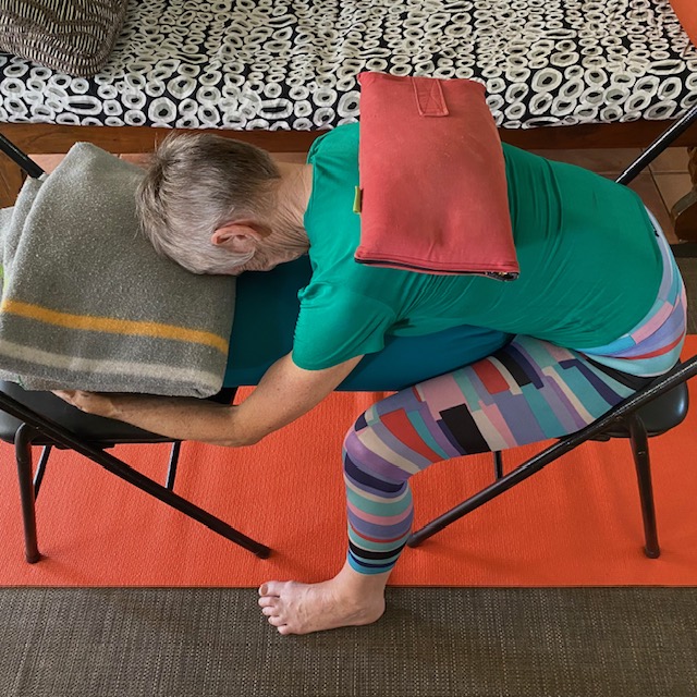 Sandbags in yoga: a sandbag across the upper back in a seated forward bend over a chair