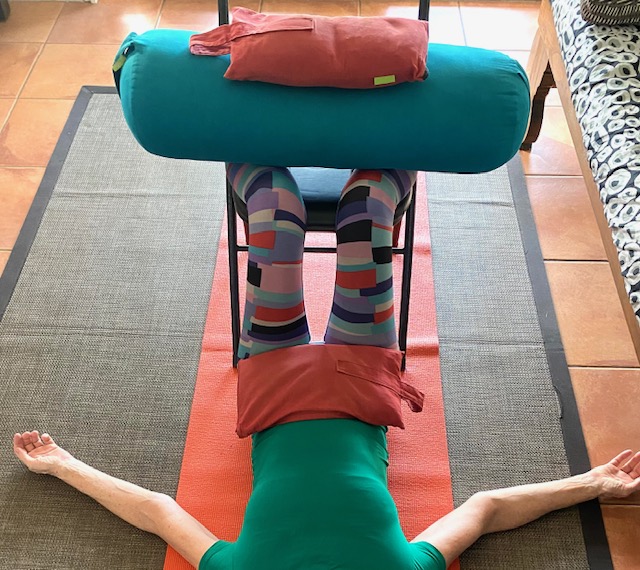 Restorative yoga props: sandbags on the feet and pelvis with the legs resting on a chair and bolster