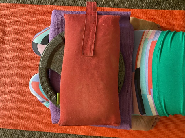Yoga props: a red yoga sandbag beside a weight plate on a mat